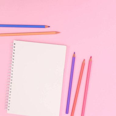 PAstel wooden pencils with open notebook copy space on pastel pink background. Flat lay