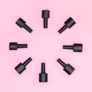 Black nail polish bottles in circle on pastel pink background with copy space. Flat lay
