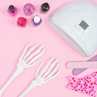 Manicure set with creative skeleton hands on pastel pink background. Flat lay