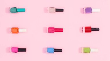 Nail polish bottles in various colors  make patern on pastel pink background. Flat lay