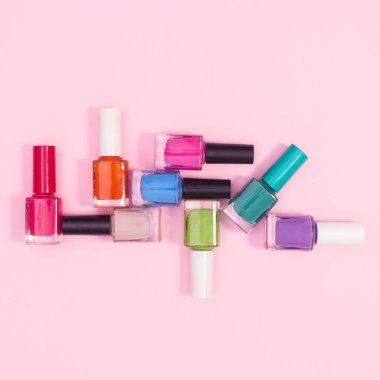 Creative composition of nail polish bottles in various colors on pastel pink background. Flat lay