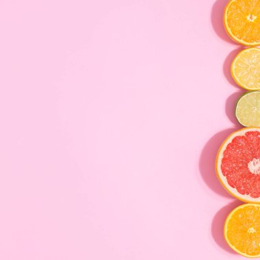 Pastel pink background with sliced citrus fruits on right side. Copy space flat lat. Summer concept