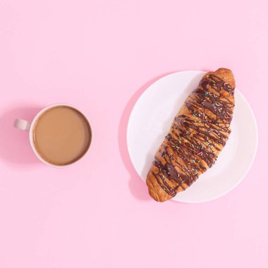 Fresh delicious croissant with chocolate and with cup of coffee on pastel pink background. Flat lay