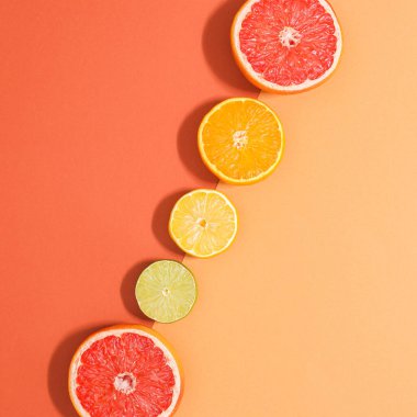 Two shade orange background with sliced citrus fruits in line. Summer fruits concept. Flat lay