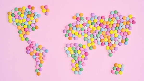 World map made with colorful candies on pastel pink bakcgorund. Flat lay. Concept Earth