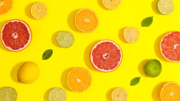 Summer pattern with sliced citrus fruits and green leaves on yellow background. Flat lay