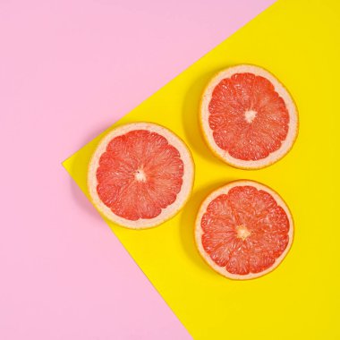 Sliced red grapefruits arrangement on pastel pink and yellow background. Flat lay