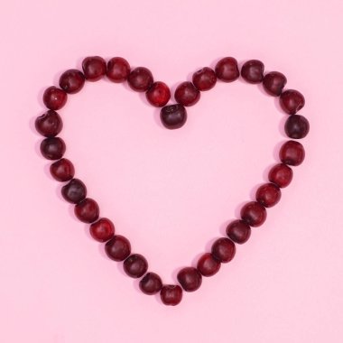 Hearg shape made with red cherries on pastel pink background with copy space. Flat lay