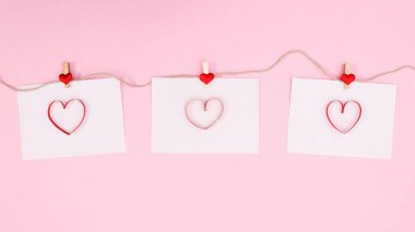 Romantic papers with hearts hanged on rope on pastel pink background. Flat lay copy space