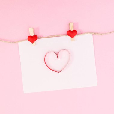 Romantic paper with heart hanged on rope on pastel pink background. Flat lay