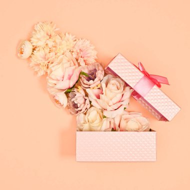 Open pastel pink gift with flowers on pastel orange background. Flat lay