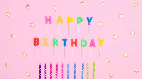 Happy birthday text with candles and stars on pastel pink background. Flat lay