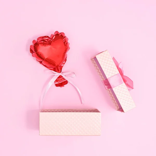 Open pastel pink gift with red ballon on pastel pink background. Flat lay
