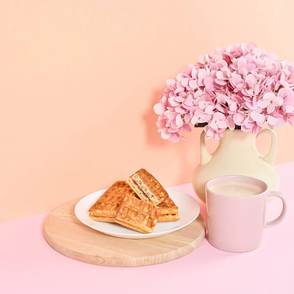 Sweet dessert waffles with bouquet of flowers in vase and cup of coffee on the table