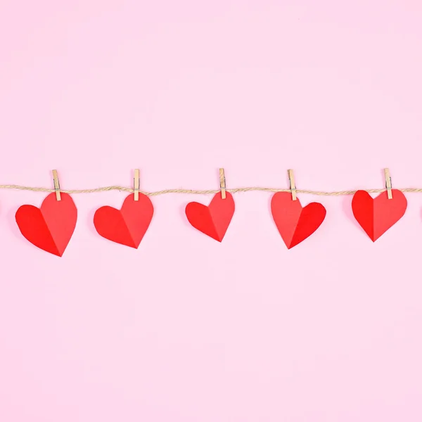 Creative hearts hanged on rope on pastel pink background. Creative Valentine\'s day concept