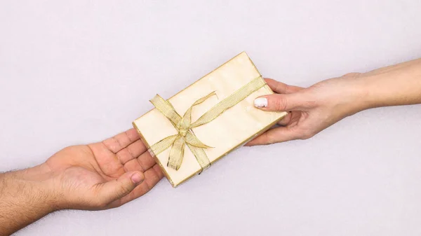 Woman hand gives to man hand golden gift with ribbon. Christmas holidays concept