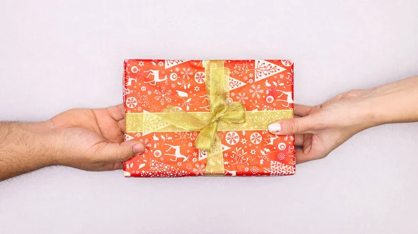 Man hand gives to woman hand red gift with golden ribbon for Christmas. Flat lay