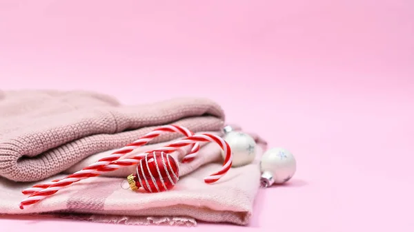 Pastel pink winter cap and skarf with Christmas ornaments on pastel pink background. New years holidays concept copy space