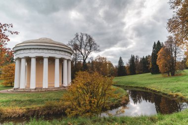 Öğleden sonra nehir kenarındaki bir sonbahar parkında sütunları olan bir kubbe şeklinde eski bir bina. Pavilion Dostluk Tapınağı. Pavlovsk 'ta. Rusya