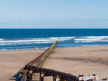 Outfall pipe at Cambois, Northumberland, UK into blue sea with wind turbines in the distance.