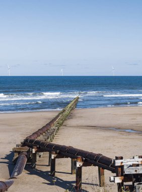 Outfall pipe at Cambois, Northumberland, UK into blue sea with wind turbines in the distance.