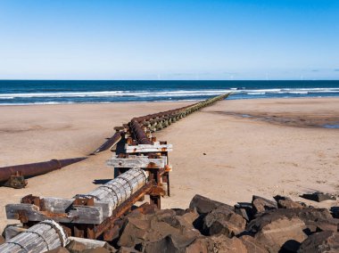 Outfall pipe at Cambois, Northumberland, UK into blue sea with wind turbines in the distance.