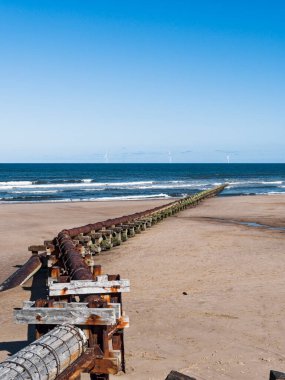 Outfall pipe at Cambois, Northumberland, UK into blue sea with wind turbines in the distance.