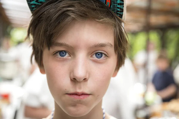 Young boy with basecap looking into the camera, blurred people i — Stock Photo, Image