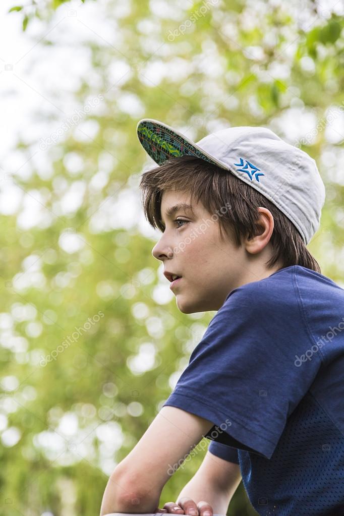 profile of a young boy with basecap and blurred green leafs in b