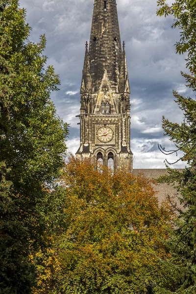 Old church steeple in stormy weather, behind some autumn trees — ストック写真