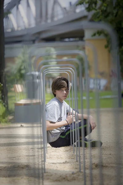 Portrait of a teenager boy sitting behind a metal frame — Stock Photo, Image