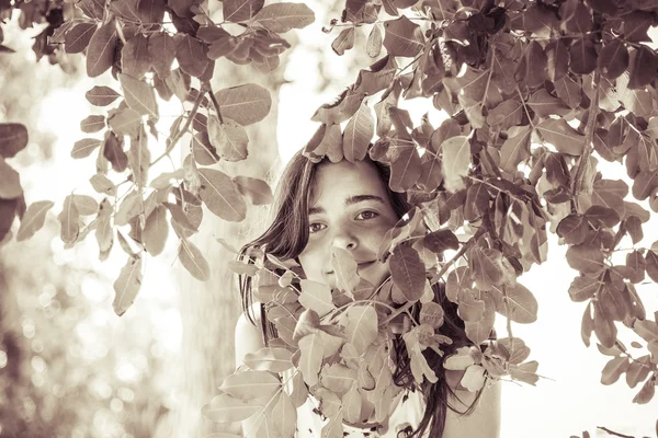 Vintage like portrait of a female teenager behind some leafs — Stock Photo, Image