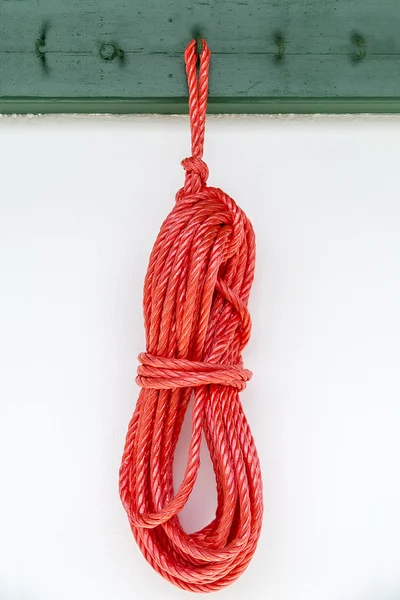 Corde rouge accrochée à un crochet vert sur un mur blanc — Photo