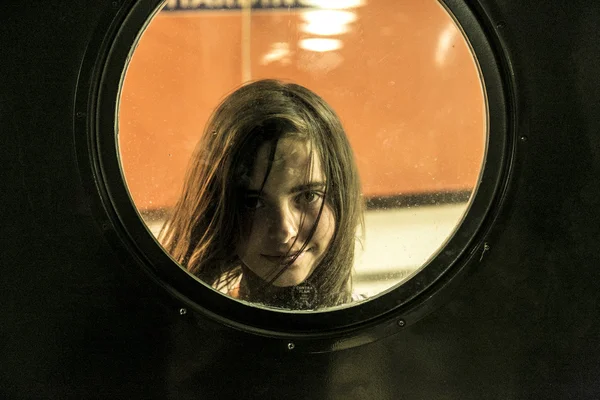 Chica mirando a través de una ventana redonda — Foto de Stock