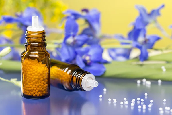 Zwei Flaschen mit Homöopathie-Kügelchen und Blüten, mit blauem Reflex — Stockfoto