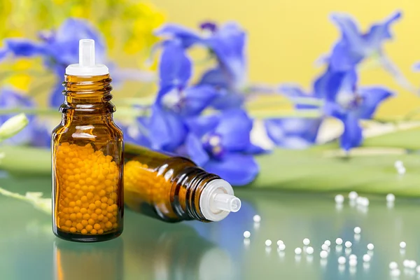 Zwei Flaschen mit Homöopathie-Kügelchen und Blumen, mit grünem Ref — Stockfoto