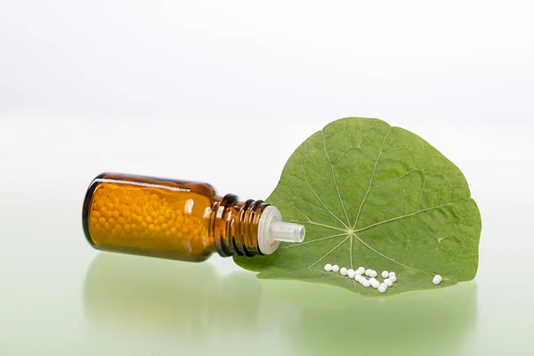 Fles met homeopathie bolletjes en groen blad — Stockfoto