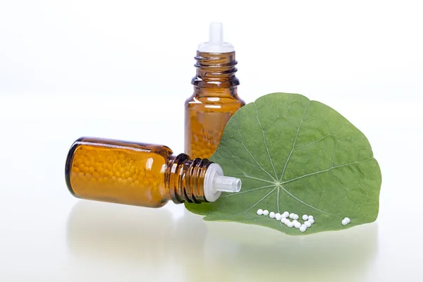 Twee flessen met homeopathie bolletjes en groen blad — Stockfoto