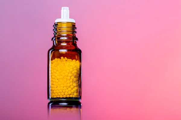 Einzelflaschen mit Homöopathie-Kügelchen, weiß-roter Hintergrund — Stockfoto