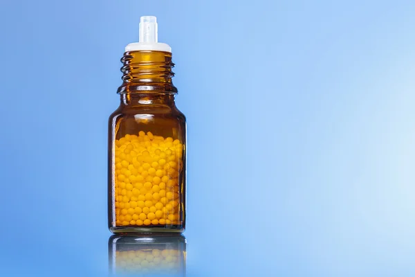 Einzelflasche mit Homöopathie-Kügelchen mit blauem Hintergrund — Stockfoto