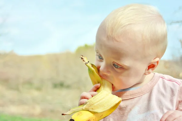Ребенок ест банан на улице — стоковое фото