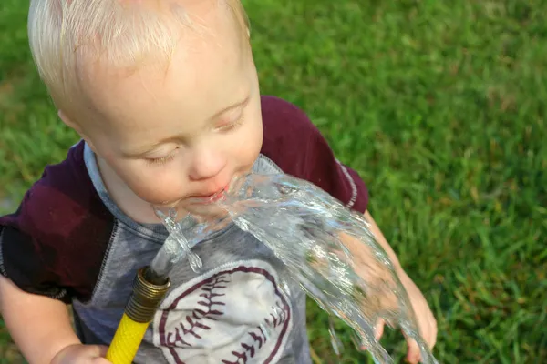 Baby trinkt Wasser aus Schlauch — Stockfoto