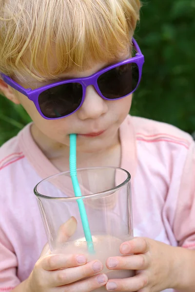 Дитина в сонцезахисних окулярах п'є шоколадне молоко — стокове фото