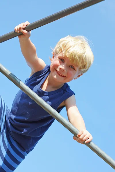 Lyckligt barn klättring på lekplats framför blå sommarhimmel — Stockfoto