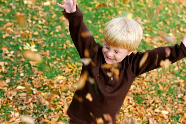 Feliz niño pequeño jugando afuera en las hojas caídas — Foto de Stock