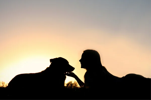 Silhouette eines Mädchens, das mit ihrem Hund im Gras liegt — Stockfoto