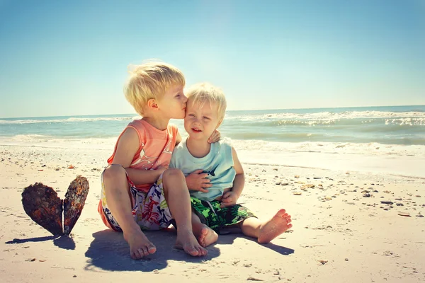 Gran Hermano besando a un niño pequeño en la playa — Foto de Stock