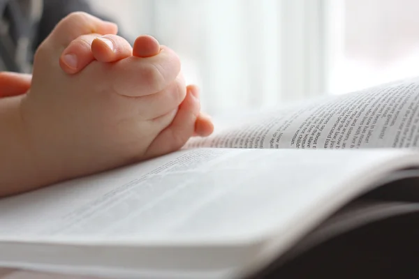 Las manos de un niño pequeño orando sobre la Santa Biblia —  Fotos de Stock