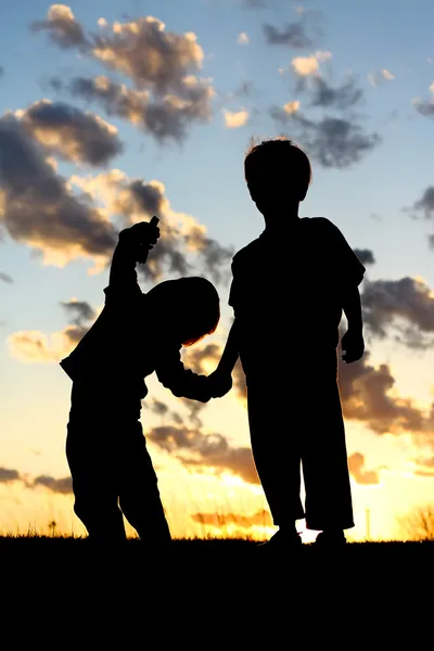 Силует дітей молодшого віку, тримаючись за руки на заході сонця — стокове фото