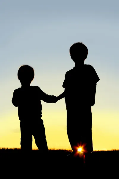 Silhueta crianças segurando as mãos ao pôr do sol — Fotografia de Stock